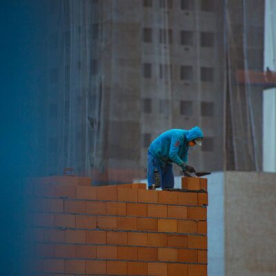 Side view of unrecognizable male in hoodie building brick wall while working on construction site in city
